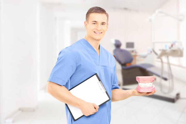 Male dentist surgeon holding dentures at his workplace