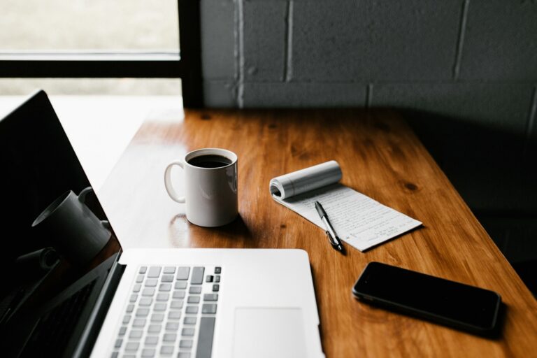 MacBook Pro, white ceramic mug,and black smartphone on table photo